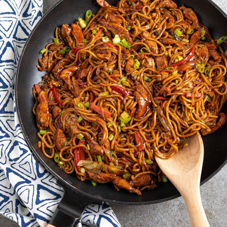 a wok filled with noodles and meat on top of a table