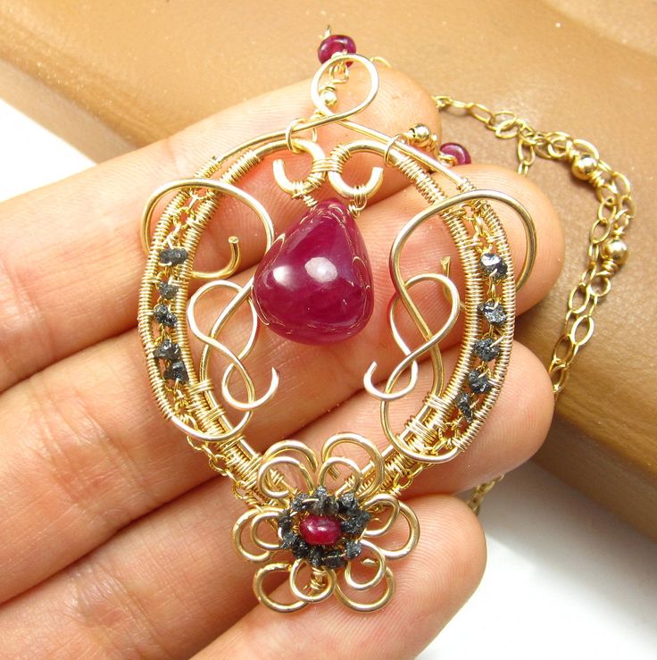 "An intricate frame of 14k gold filled wire has been constructed from various gauges of wire and pain-stakingly wrapped together in this design. Crawling along the sides of the frame are rich and rough black DIAMOND chips. The flower at the bottom of the pendant has a ruby encircled by these rough diamonds as well. The center focal of this piece is a BOLD and BIG RUBY briolette, Which is clear and uniform enough to glow when the light hits it. This stone measures about 17 mm long by 15 mm wide. Elegant Copper Wire Pendant Jewelry, Gold Wire Wrapped Freeform Jewelry, Gold Freeform Wire-wrapped Jewelry, Gold Freeform Wire Wrapped Jewelry, Artisan Freeform Gold Jewelry, Gold Gemstone Jewelry With Copper Wire, Gold Copper Wire Jewelry With Gemstones, Elegant Gold Necklace With Copper Wire, Elegant Freeform Wire Wrapped Jewelry