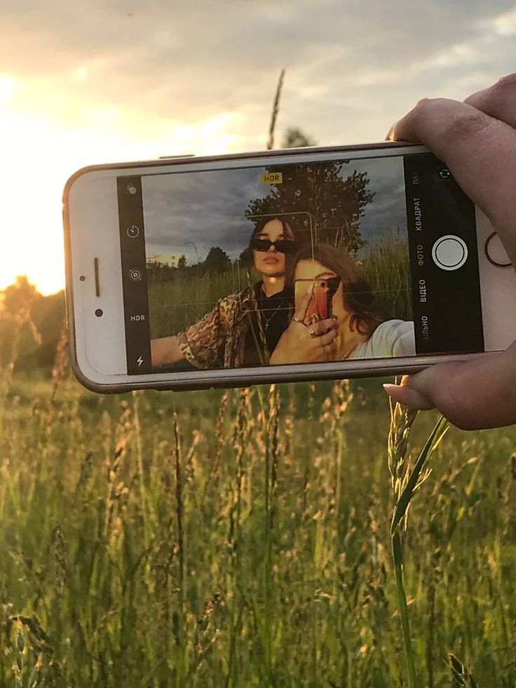 a person taking a photo with their cell phone in a grassy field at sunset or sunrise