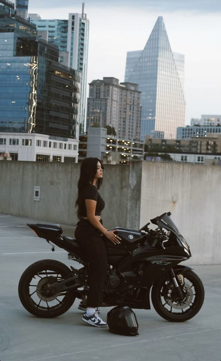 a woman sitting on top of a motorcycle in front of some tall buildings and skyscrapers