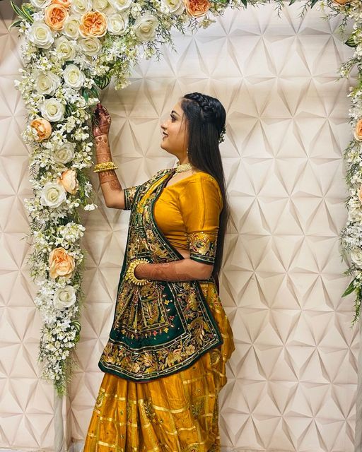 a woman in a yellow and green sari standing next to a white flower arch