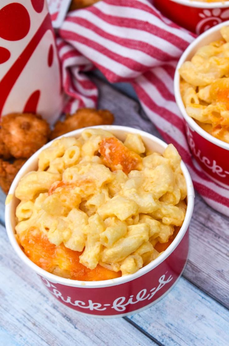 two red bowls filled with macaroni and cheese next to fried chicken nuggies