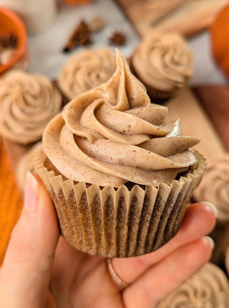 a person holding a cupcake with frosting on it in front of other cupcakes