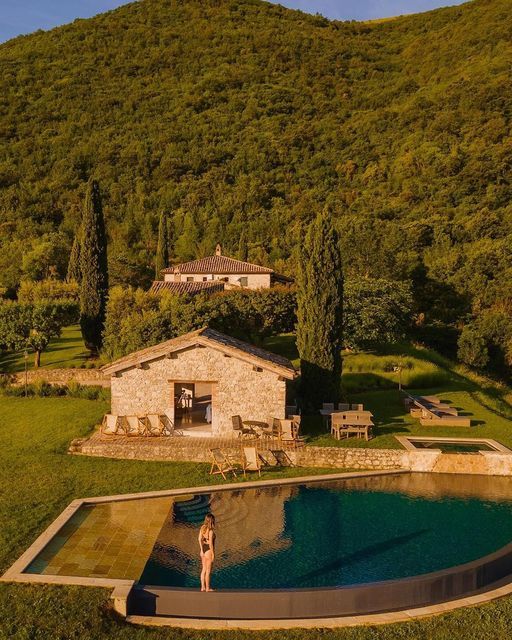 a woman standing in the middle of a pool surrounded by trees and mountains with a house behind it