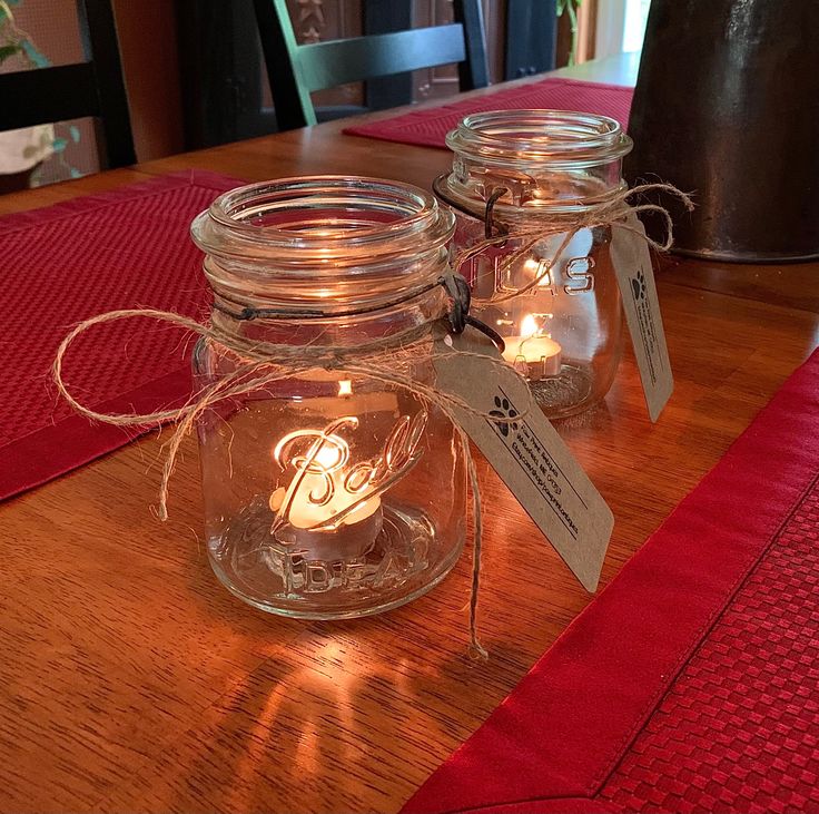 two mason jars are sitting on a table with lights in the jar and tags attached to them