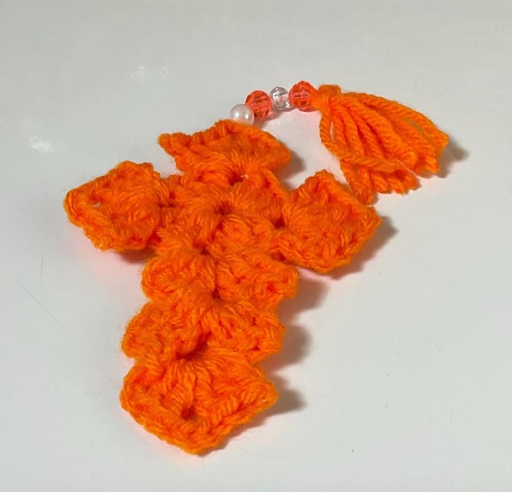 an orange crocheted flower with beads on it's end is laying on a white surface