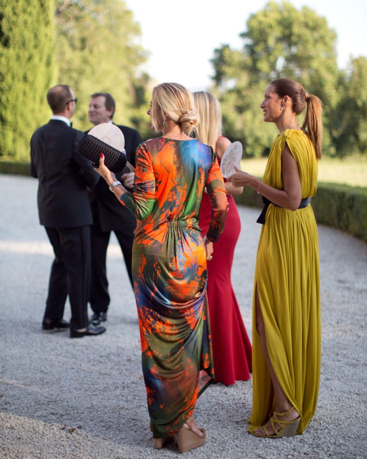 two women in long dresses talking to each other while others stand around and look on