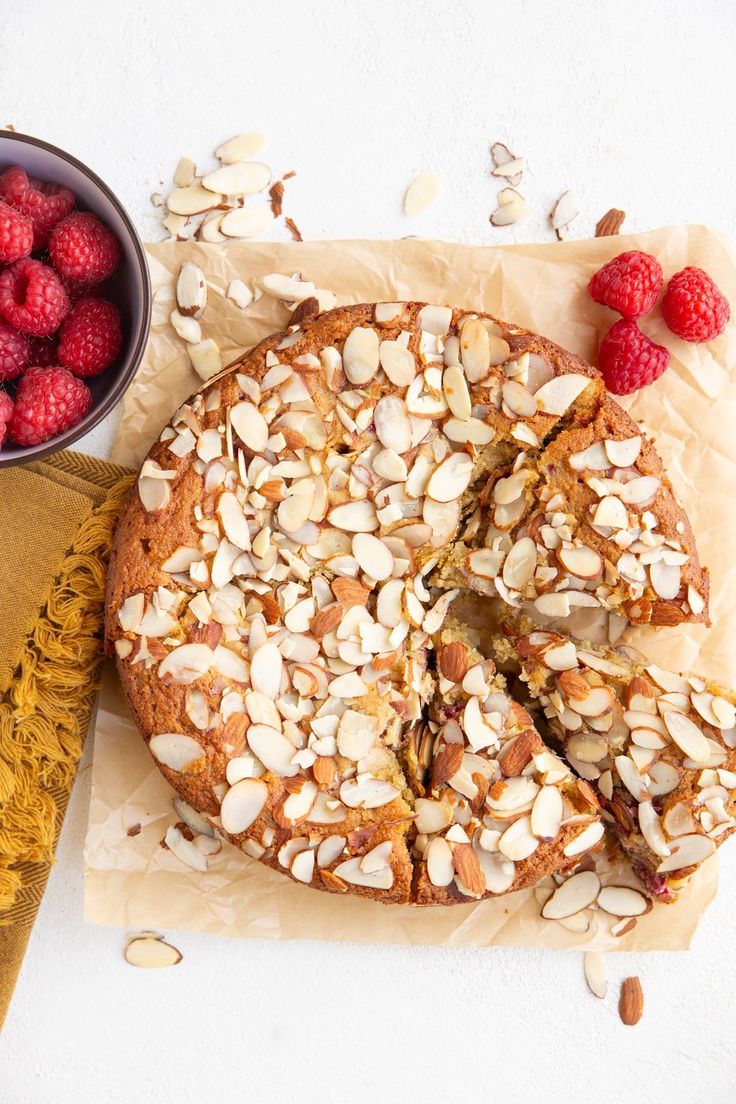 a cake with almonds and raspberries on it next to a bowl of raspberries