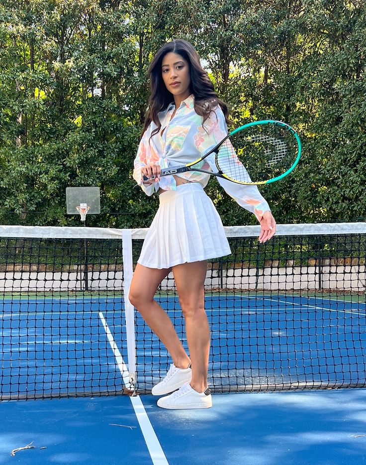 a woman holding a tennis racquet on top of a tennis court with trees in the background