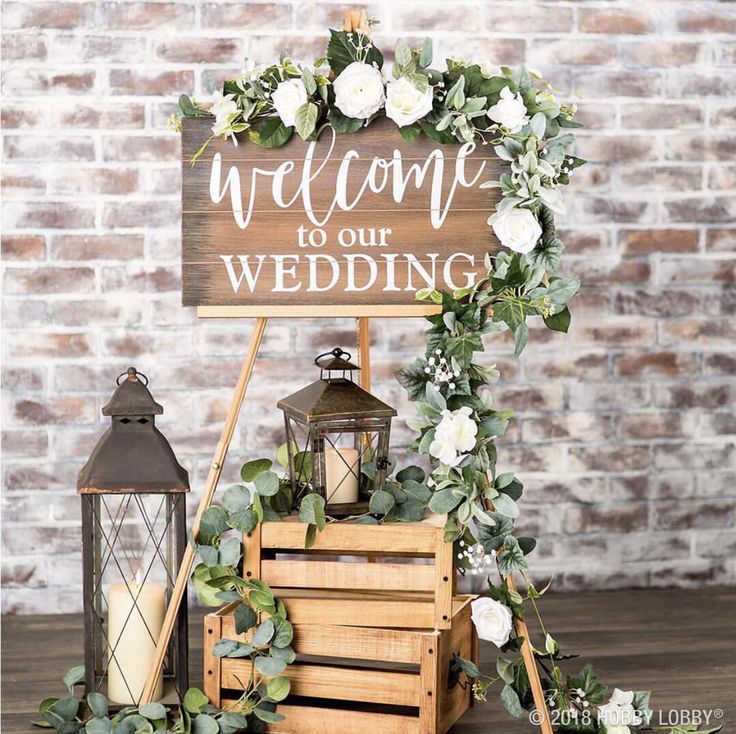 a welcome to our wedding sign with flowers and candles on it next to a brick wall