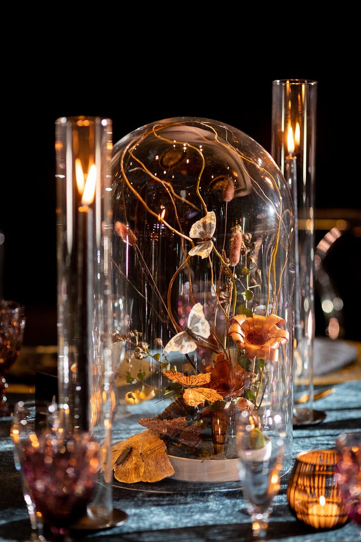 a table topped with lots of glass vases filled with flowers and plants next to candles