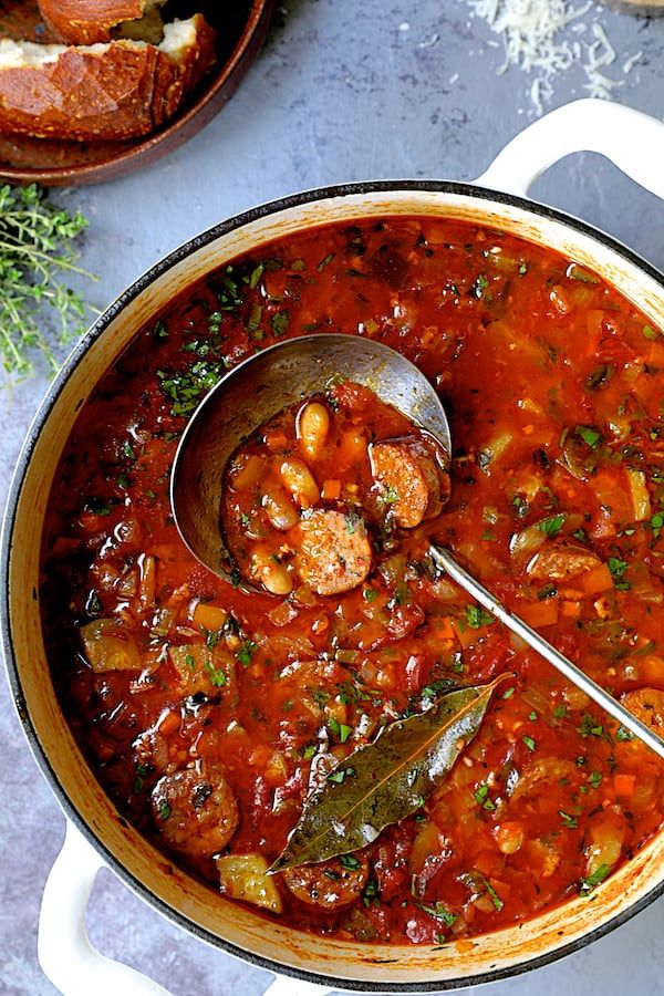 a pot full of stew with a ladle in it and bread on the side