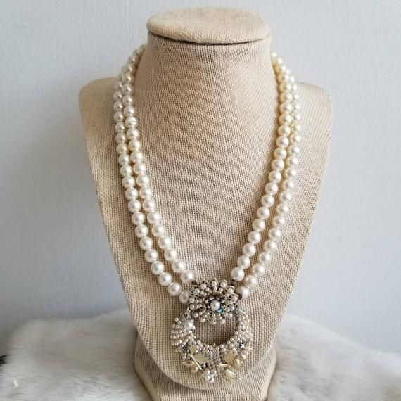 This is a vintage statement necklace from the 1950's-1960's. The necklace is made from two white pearl tone bead strands. The pendant is also the clasp of the necklace and is a white pearl tone and AB crystal statement piece. The back is a gold tone metal with the Japan signature. The necklace has a few areas of wear on the back from age. The necklace is in great condition.Measurements:Strand Length: 17" | Pendant Length: 2.25" | Pendant Width: 1.75"Unless otherwise stated all vintage items are Vintage Pearl-embellished Jewelry For Formal Occasions, Vintage Pearl-embellished Jewelry For Formal Events, Vintage Pearl Embellished Jewelry For Formal Occasions, Vintage Pearl White Pearl Chain Jewelry, Vintage Pearl White Pearl Jewelry, Vintage Pearl Charm Jewelry For Anniversary, Vintage Jewelry With Pearl Charm For Anniversary, Vintage Pearl Embellished Jewelry Gift, Vintage Pearl Beaded Necklace With Pearl Charm