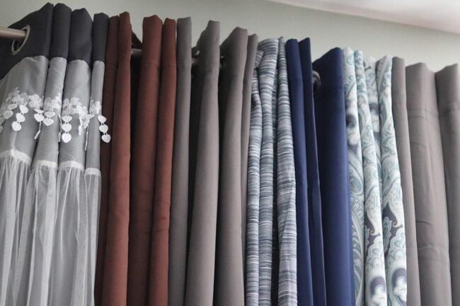 many different colored fabrics are hanging on the wall in front of a window with an open curtain