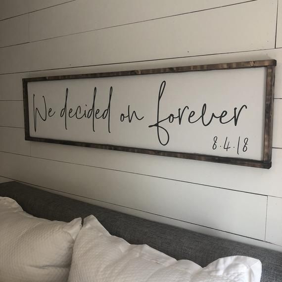 a wooden sign that says we decided on forever above a bed with white sheets and pillows