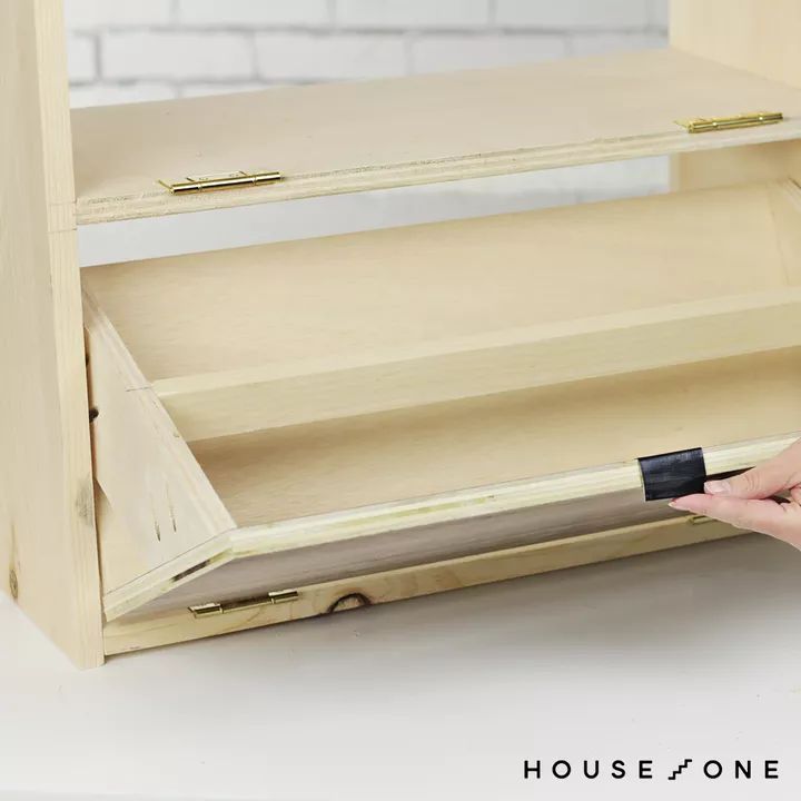 a person holding a piece of wood in front of a wooden cabinet with the door open