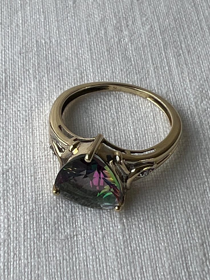 Lots of flash and colour in this lovely 14K yellow gold and trilliant cut mystic topaz ring.   Single diamonds on either side of the topaz offer a bit more subtle sparkle.  The only mark on the band is an R in a circle.  Both diamonds and topaz tested on my gem tester, the gold has been jeweller tested as 14K.  On my mandrel the ring fits to size approx. 6.5 (halfway between 6 1/2 - 6 3/4)  I try to provide as much information as possible about the size of a ring but if more measurements are nee Gold Topaz Multi-stone Ring, Elegant 14k Gold Multi-stone Topaz Ring, 14k Gold Multi-stone Topaz Ring, Mystic Topaz Earrings, Mystic Topaz Ring, Mystic Topaz, Ring Fit, Topaz Ring, Ring Box