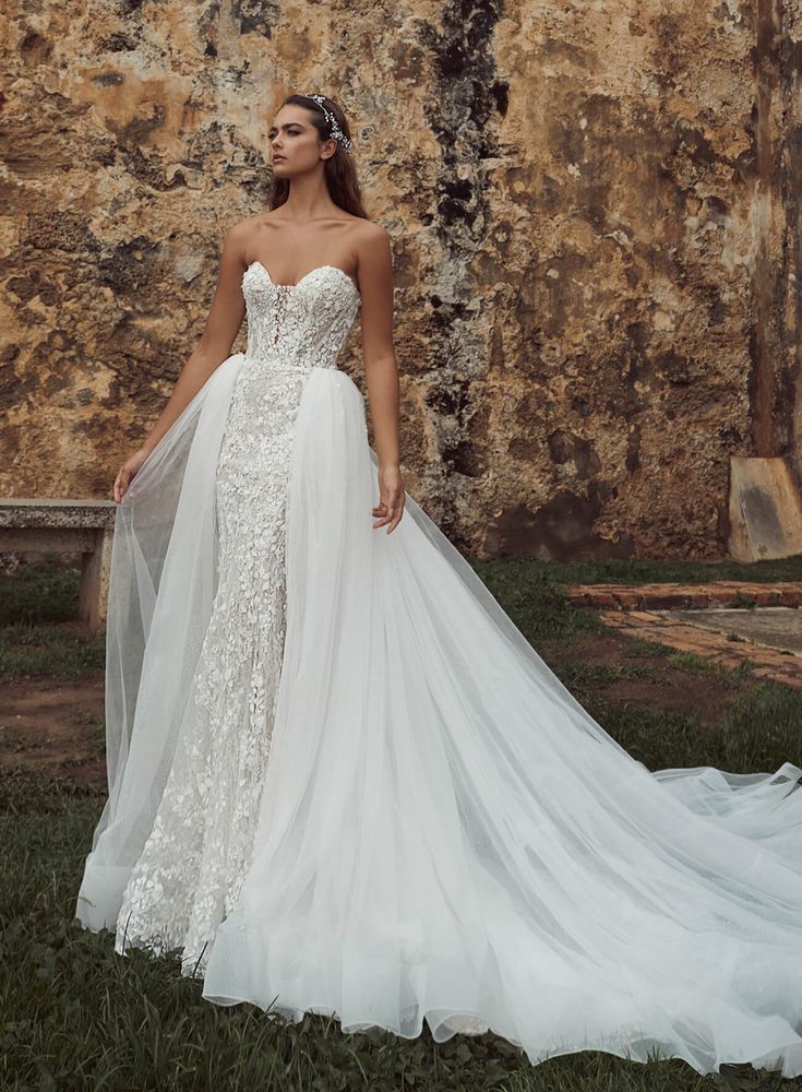 a woman in a wedding dress standing on the grass near a stone wall and wearing a veil