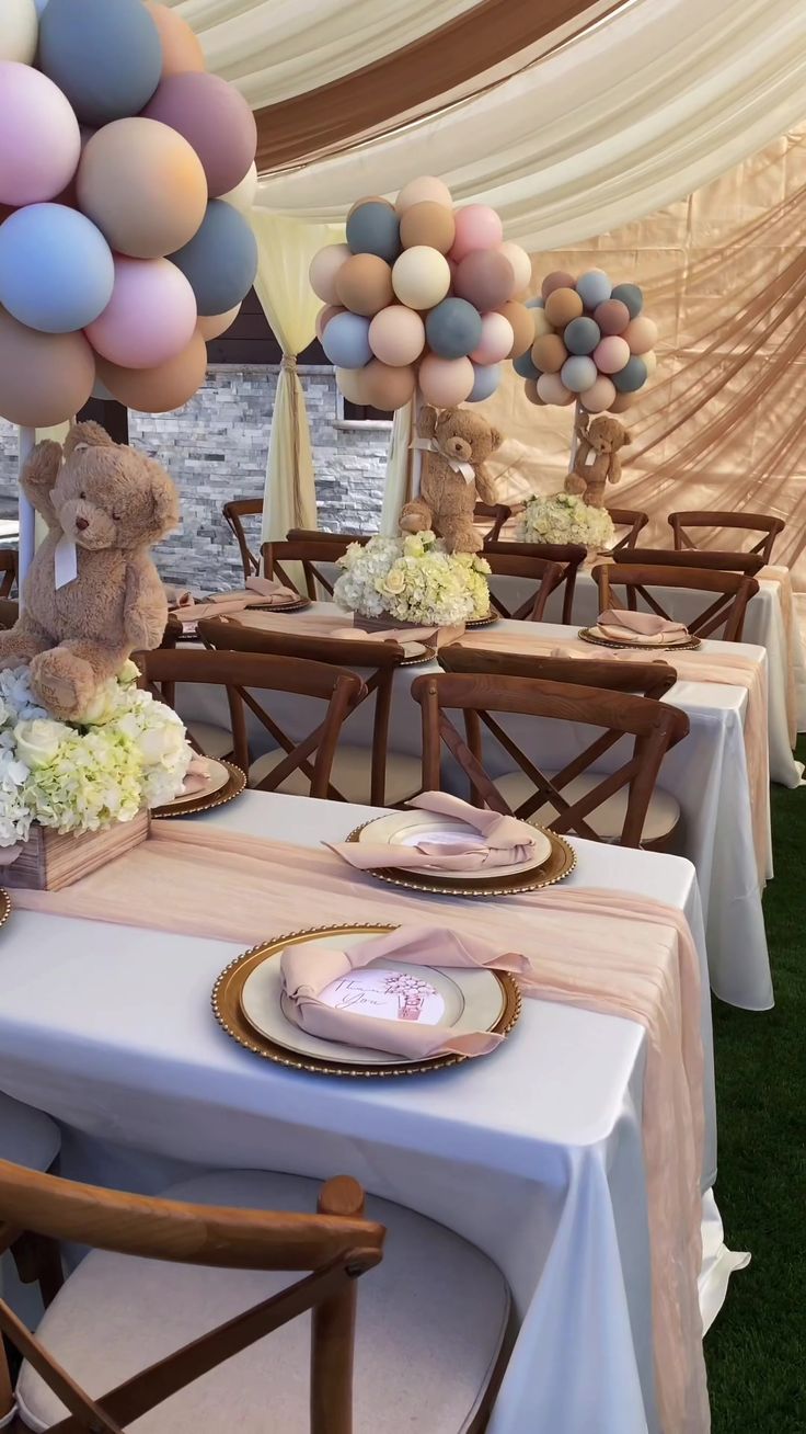 a table set up for a baby shower with teddy bears and balloons in the background