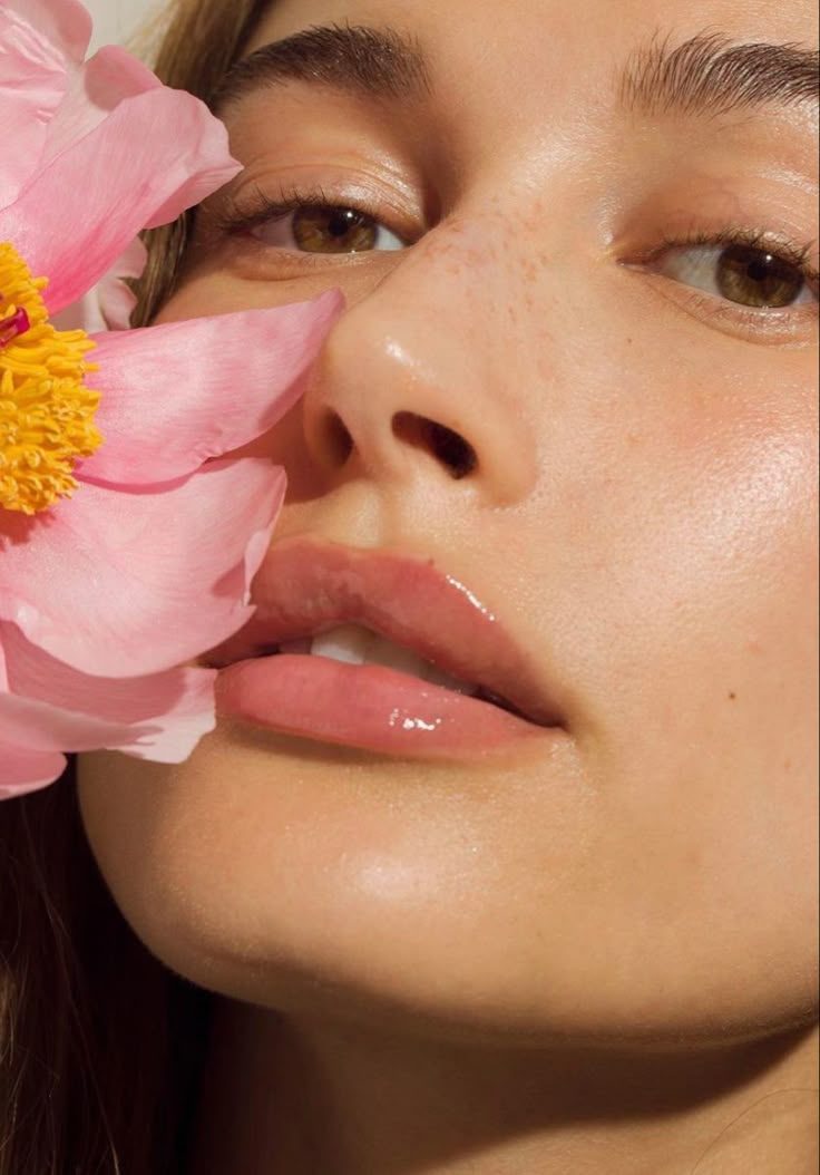 a close up of a woman holding a flower to her face and looking at the camera