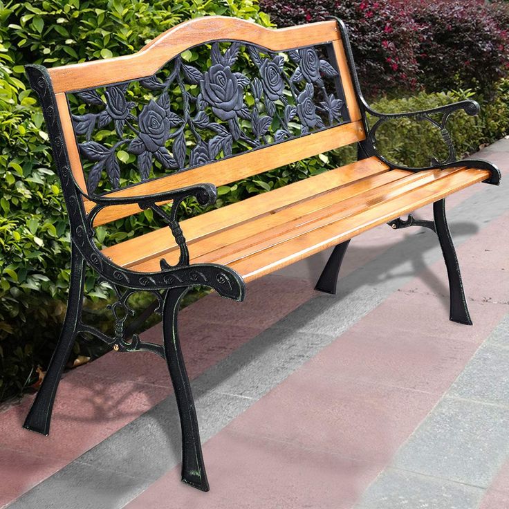 a wooden bench sitting on top of a sidewalk next to green bushes and shrubbery