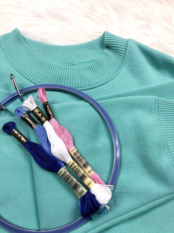 three different colored threads and scissors on a blue t - shirt with a circular frame