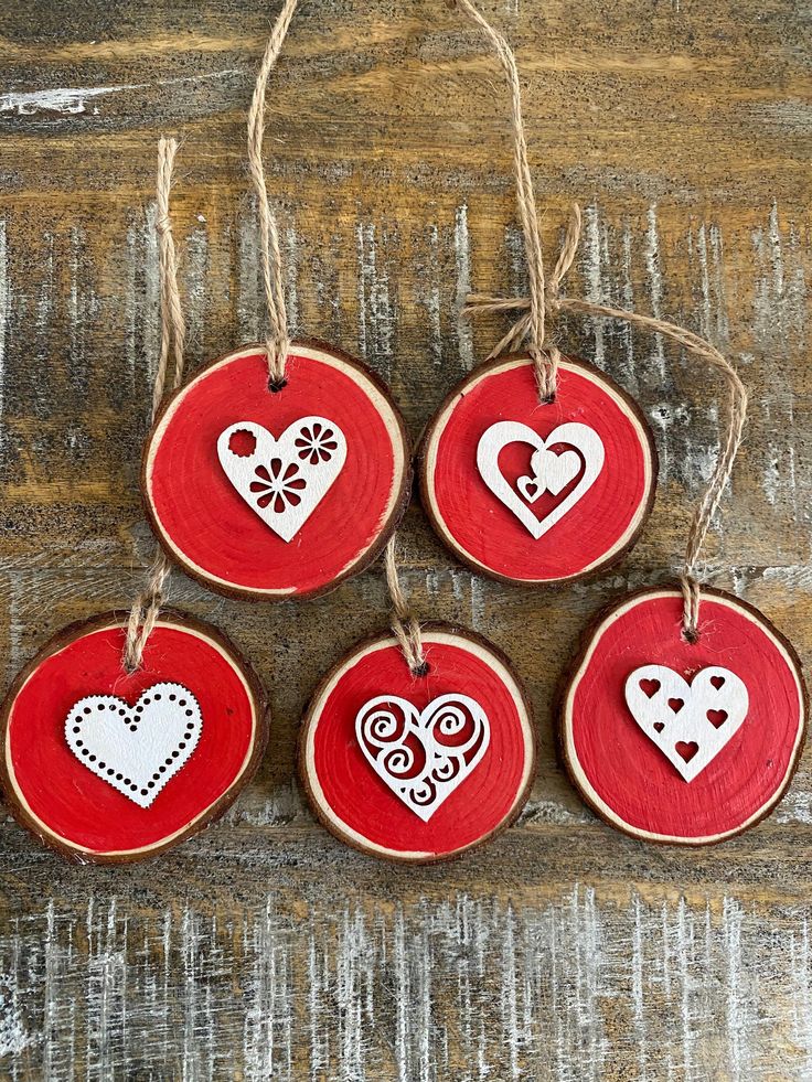 four red and white heart ornaments hanging from twine on wood planks with string