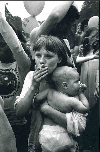 a woman holding a baby in her arms surrounded by other people at an outdoor event