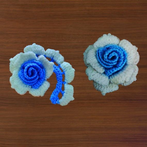 two crocheted blue and white flowers sitting on top of a wooden table next to each other