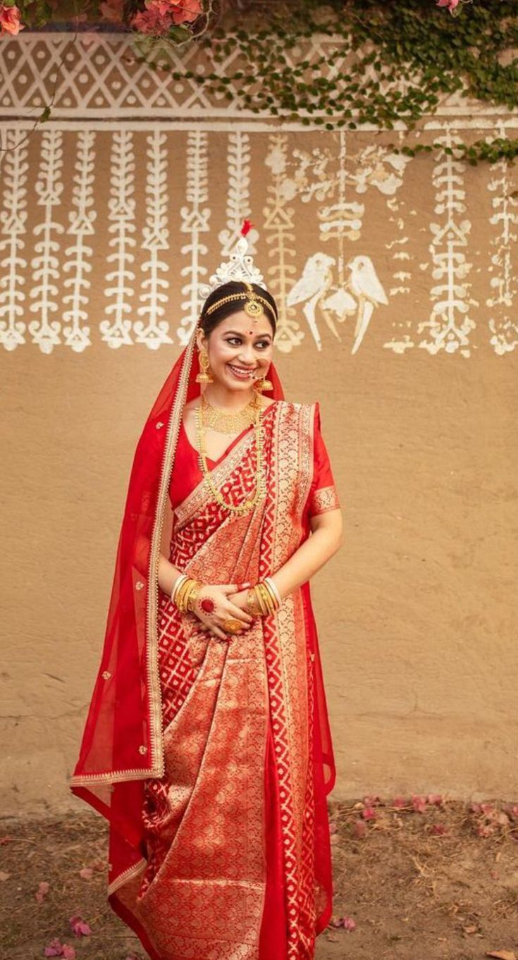 a woman wearing a red and gold bridal outfit standing in front of a wall