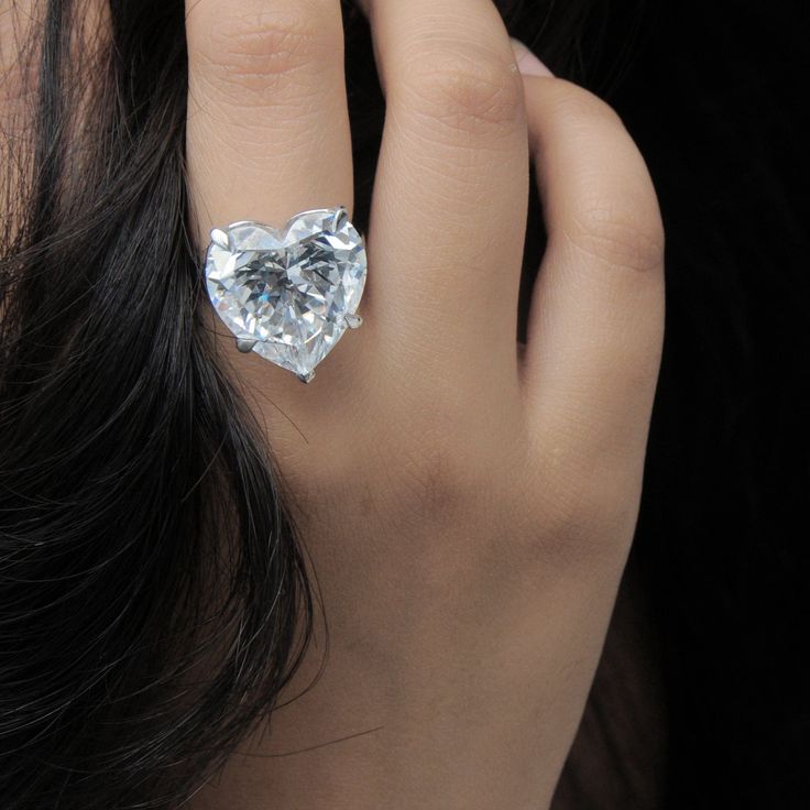 a close up of a person wearing a ring with a heart shaped diamond on it