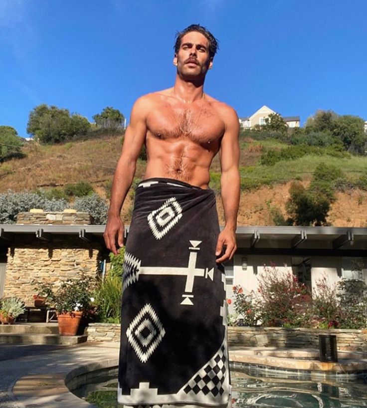 a shirtless man standing in front of a pool with his towel draped around him