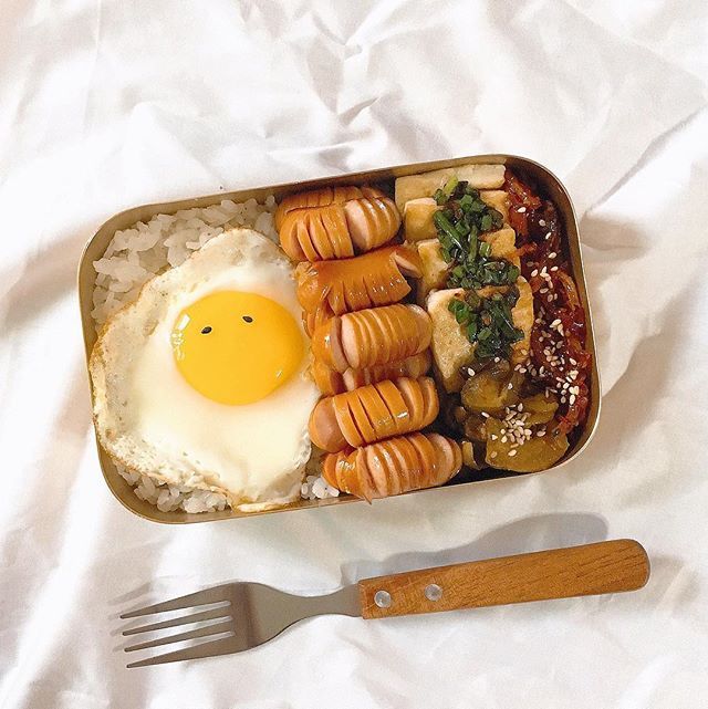 a bento box filled with rice, meat and an egg sitting on top of it