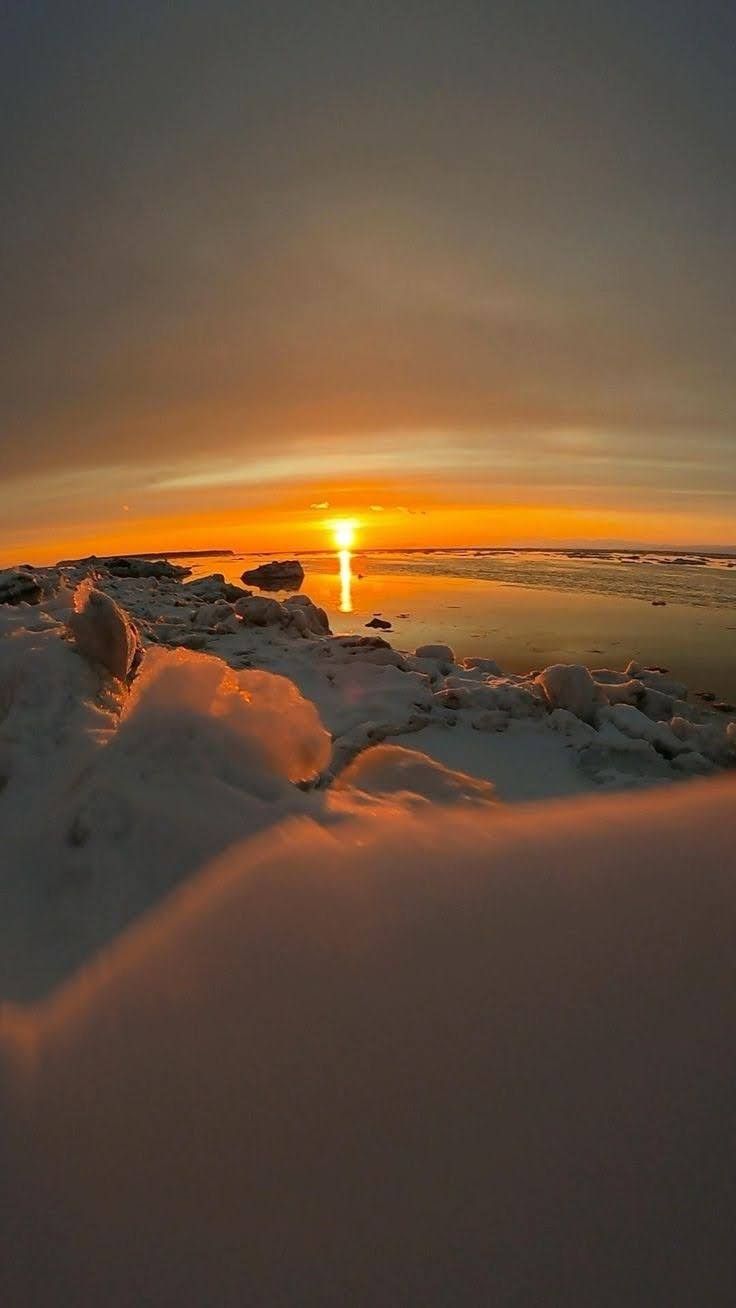 the sun is setting over some ice covered rocks and water with snow on it's sides