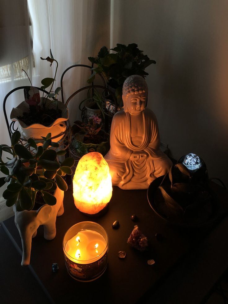 a buddha statue sitting on top of a table next to candles and other items in front of a window