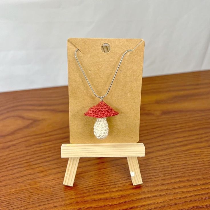 a small wooden stand holding a red and white mushroom necklace on it's side