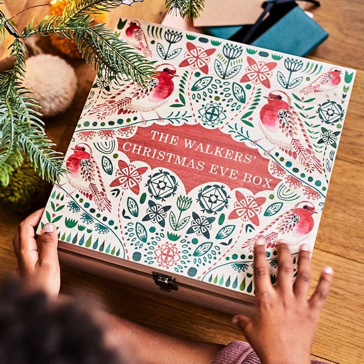 a person holding a christmas eve box on top of a wooden table next to a tree