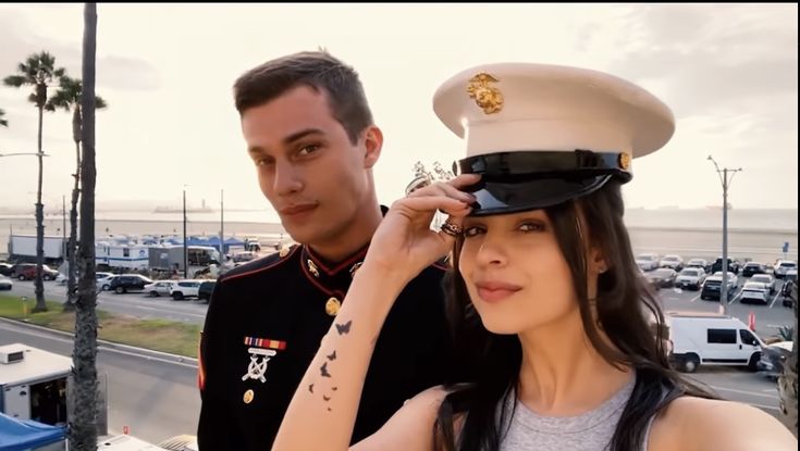 a man in uniform saluting to a woman on the side of the road with palm trees behind her