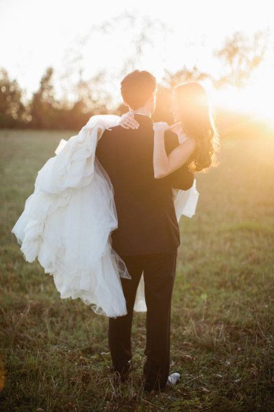 a bride and groom are standing in a field at sunset with the sun behind them