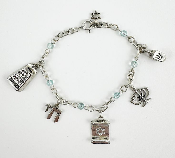 This stunning Jewish silver charm bracelet is a perfect gift or way to show your Jewish heritage, and support for Israel.  With five unique charms that represent important aspects of Jewish culture. The Tzedakah Box charm represents the importance of giving, while the Chai charm symbolizes life. The Torah charm represents knowledge, and the Menorah charm symbolizes the Festival of Lights. Lastly, the Dreidel charm represents the joy of Hanukkah. Celebrate your love for Jewish culture with this beautiful bracelet that is sure to spark conversation and admiration. The bracelet is adjustable to fit most wrists, and is made with high-quality materials that will last for years to come.  - Bracelet Size: 7 inches length  - Charm Size: 1/2 inch  - Light Turquoise Beads  - Spring Ring Clasp - Silv The Torah, Jewish Heritage, Jewish Culture, Festival Of Lights, Silver Elephants, Elephant Necklace, Silver Charm Bracelet, Menorah, Festival Lights