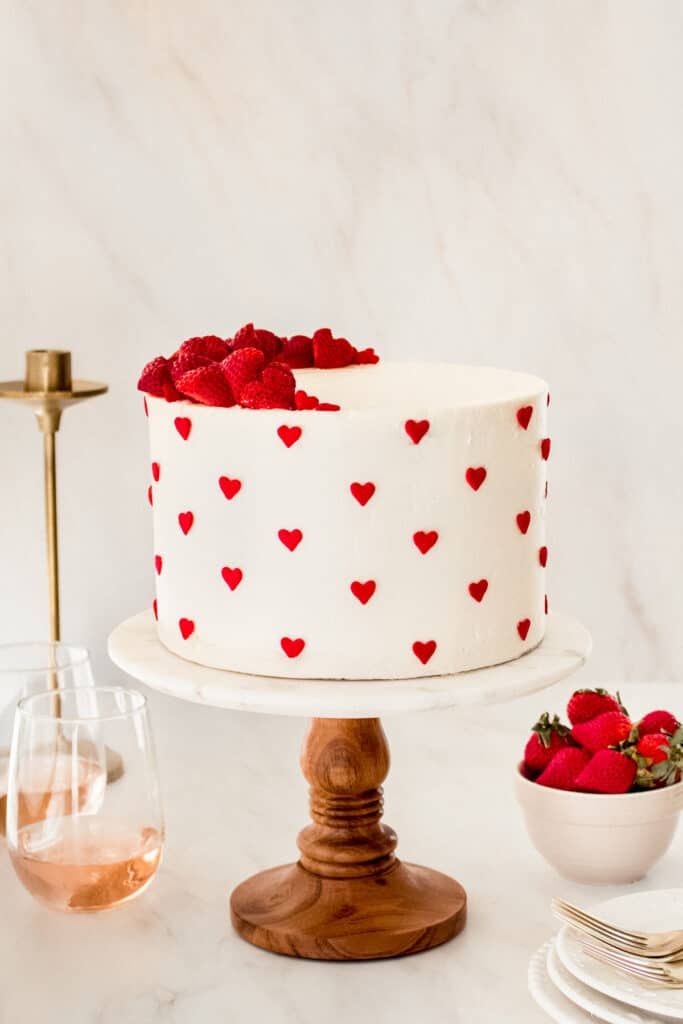 a white cake with red hearts on it sitting on top of a table next to plates and wine glasses