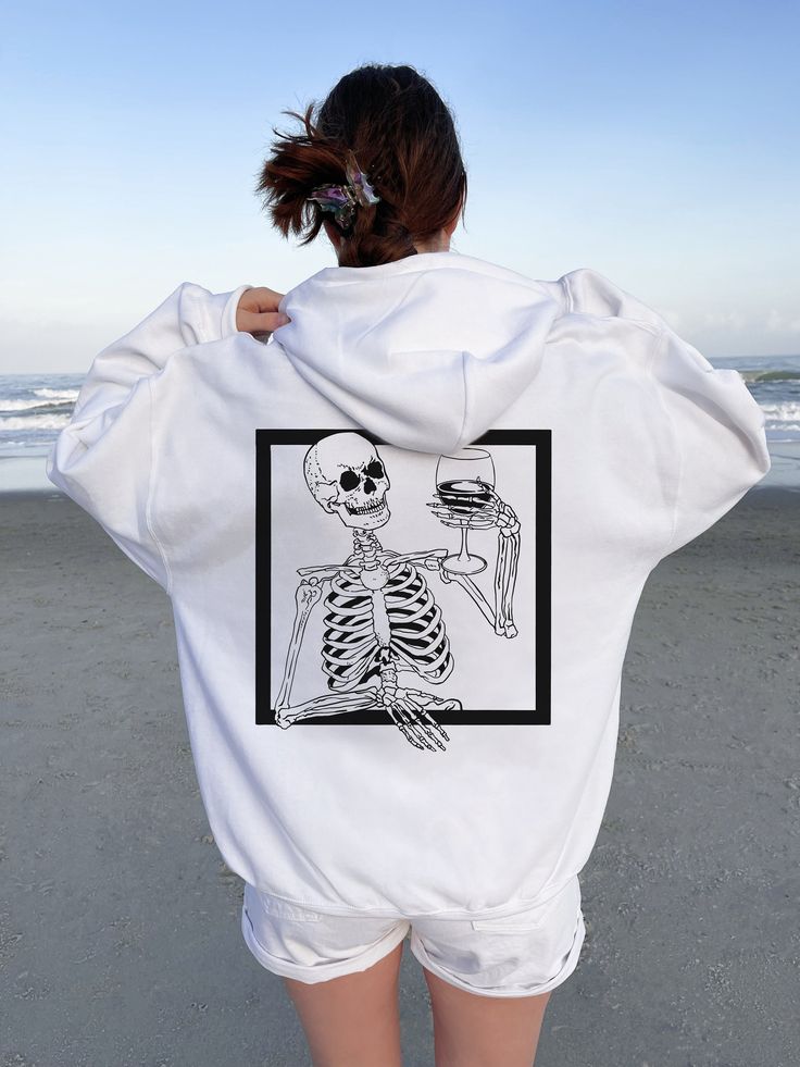 a woman standing on the beach with her back to the camera, wearing a skeleton sweatshirt