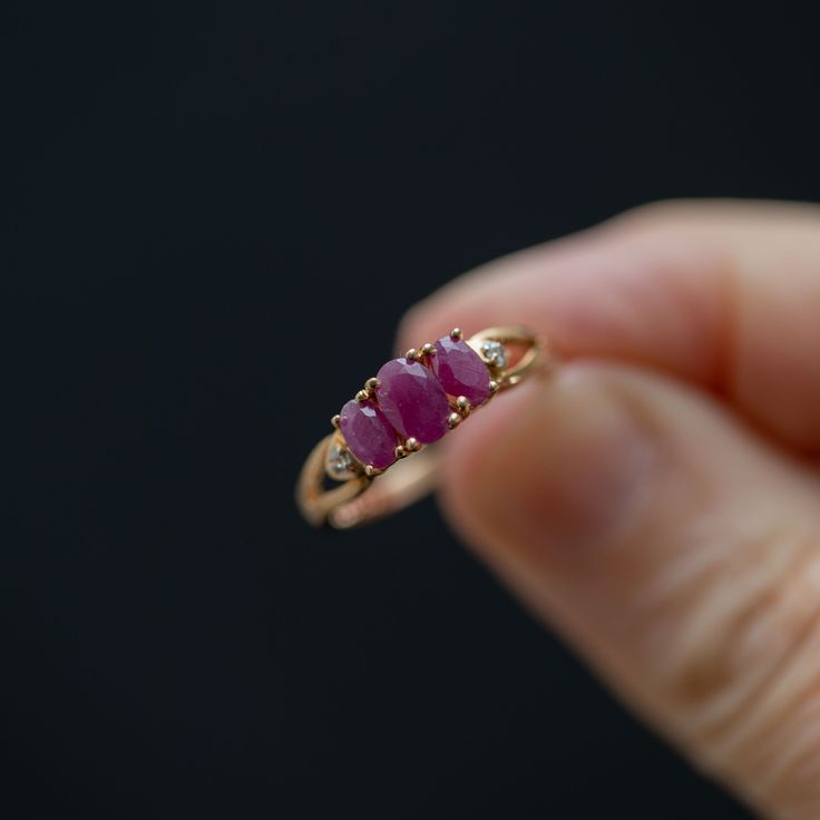 Get ready to make a statement with this stunning handmade, vintage trilogy ring crafted from high-quality 10k yellow gold. This ring boasts three magnificent pinkish red rubies and two dazzling accent diamonds that will take your breath away. The center stone measures 5.5mm x 3mm, while the two stones on either side measure 4.5mm x 3mm, all held securely in place by elegant prongs. The split shank design at the top of the ring leads down to a straight shank, ensuring a comfortable and snug fit o Ruby Trilogy Ring, Three Stone Ring Design, Classic Three-stone Ruby Ring, Classic Three Stone Ruby Ring, Red Three-stone Diamond Promise Ring, Red Three Stone Diamond Ring For Promise, Red Three Stone Diamond Promise Ring, Classic Three Stone Ruby Promise Ring, Red Three Stone Rings For Anniversary