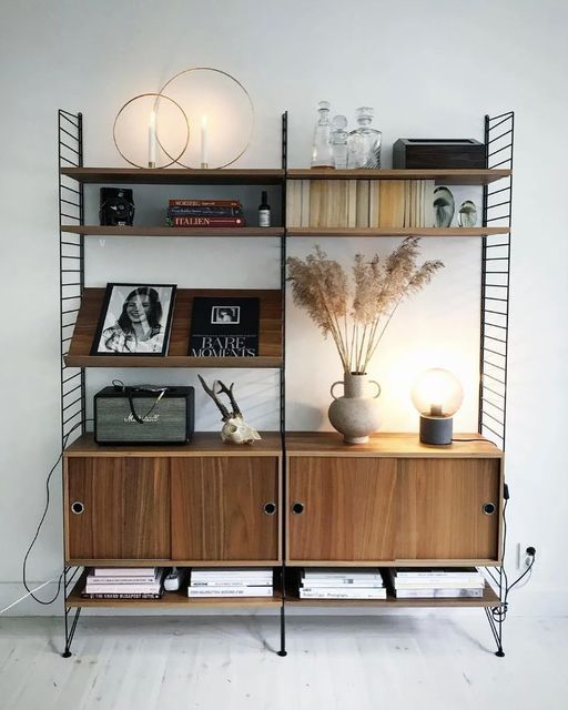 a shelf with books, vases and pictures on it in a white walled room