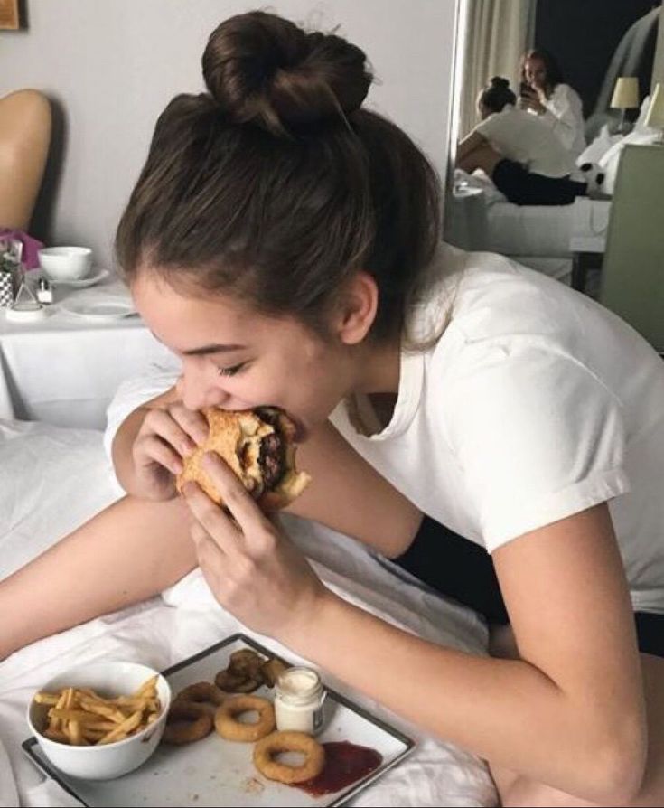 a woman sitting at a table eating a sandwich and french fries in front of her