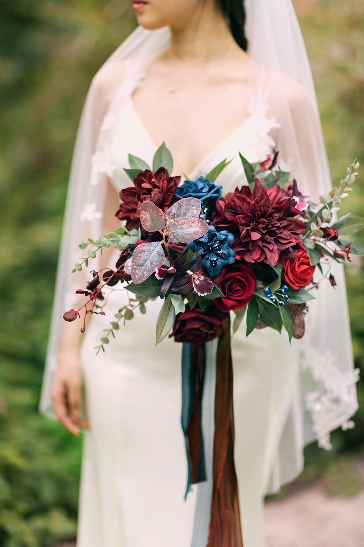 a woman in a wedding dress holding a bridal bouquet with red and blue flowers