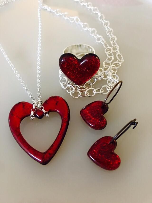 three red heart shaped necklaces and pendants on a white surface with silver chain