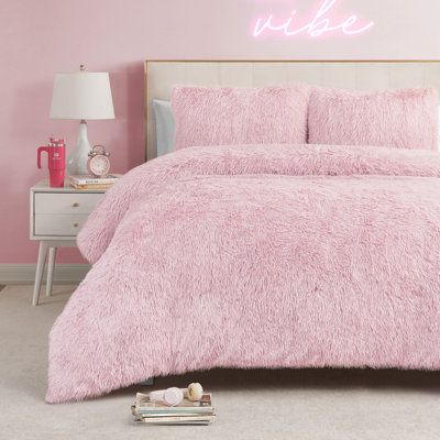 a bed with pink comforter and pillows in a bedroom next to a night stand