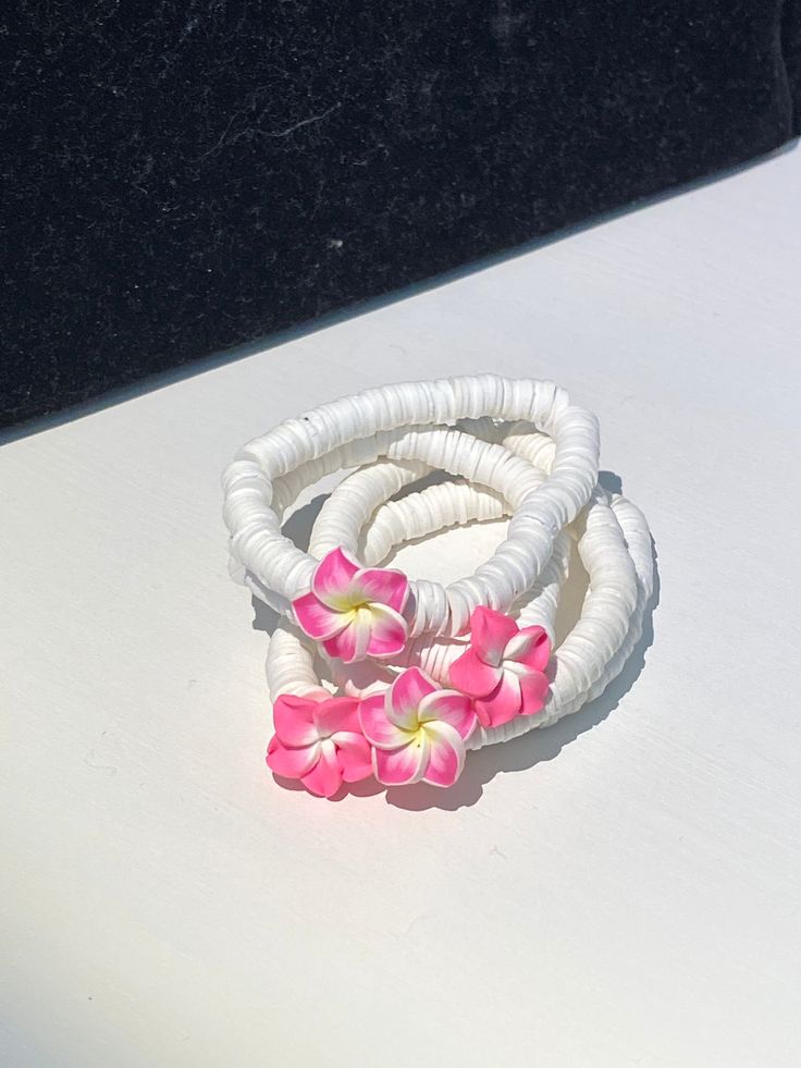 This is a white beaded bracelet with a Hawaiian flower in the center. There are 7 colors of the flower. the colors include pink and yellow, pink and white, magenta and yellow, dark purple and yellow, green and yellow, blue and yellow, white and yellow. Each bracelet is about 6-7 inches in circumference and the bracelets are stretchy. White Flower Jewelry For Vacation, White Flower Bracelets For Vacation, Bohemian Flower Bracelets For Vacation, Adjustable White Jewelry With Flower Decoration, Pink Flower-shaped Jewelry For Vacation, Pink Flower Jewelry For Vacation, Multicolor Flower Bracelets For Beach, Flower Shaped Bracelets For Beach, Flower Shaped Beaded Bracelets For Beach