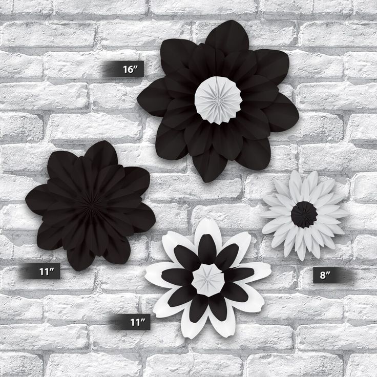 three black and white paper flowers on a brick wall with measurements for each flower size